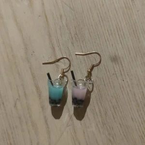 Söta örhängen med boba-te design - Unika örhängen formade som små boba-te drinkar i blått och rosa. Perfekta för att ge en lekfull touch till din outfit. De har små sugrör och detaljerade pärlor som liknar boba-pärlor. Passar både till vardags och festliga tillfällen!