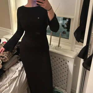 Svart långklänning med öppen rygg - Säljer en elegant svart långklänning med en fantastisk öppen rygg. Klänningen har en tight passform och långa ärmar, perfekt för festliga tillfällen. Materialet är mjukt och följsamt, vilket gör den bekväm att bära hela kvällen.