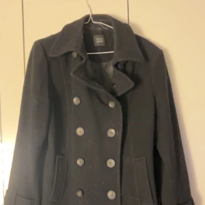 Svart kappa från DIXI COAT - Säljer en stilren svart kappa från DIXI COAT i mycket bra skick. Den har en klassisk dubbelknäppning med stora knappar och långa ärmar. Perfekt för höst och vinter, håller dig varm och snygg! 🖤