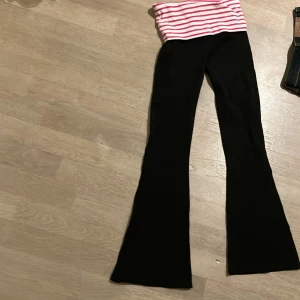 Svarta byxor med randig midja  - Säljer ett par svarta byxor med en superfin randig midja i rosa och vitt. Byxorna har en bootcut-stil som ger en snygg siluett. Perfekta för en avslappnad dag eller en mysig hemmakväll.