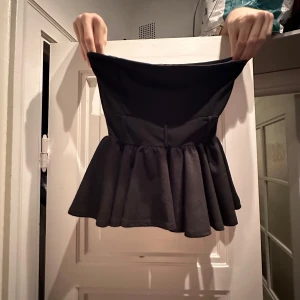 Svart kjol från Boohoo - Snygg svart tröja från Boohoo med volangdetalj. Perfekt för festliga tillfällen eller en utekväll. Materialet känns mjukt och bekvämt, vilket gör den skön att bära hela dagen.