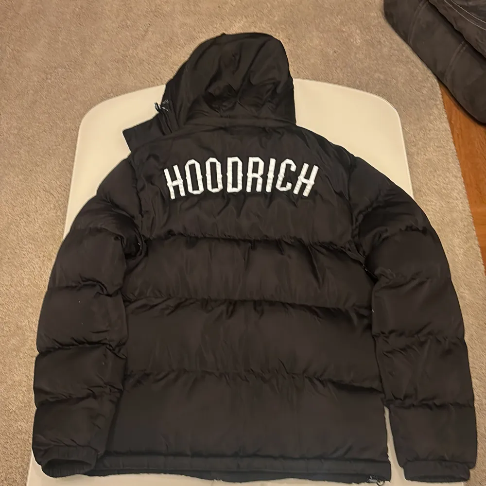 Säljer en svart dunjacka från Hoodrich i storlek XL. Jackan har en dragkedja framtill och en stor huva för extra värme. Perfekt för kalla vinterdagar. Den är i mycket bra skick och har en stilren design med Hoodrich-loggan både fram och bak.. Jackor.