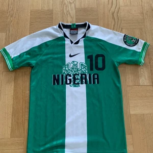 Retro Nigeria tröja! - Tröjan är väldigt skön och är i 10/10 skick. Säljer den pga för lite användning. Passar allt från 178-183 cm. Sitter bra på mig och är 181cm.  Pris kan diskuteras👌