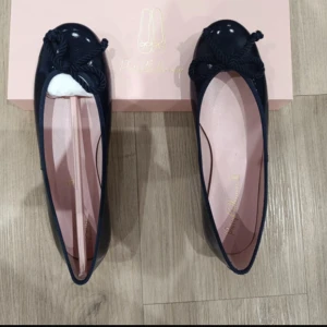 Marinblå ballerinaskor med rosett - Säljer ett par nya oanvända eleganta marinblå ballerinaskor med en söt rosett på tån. Skorna har en glansig finish och en mjuk rosa innersula. Perfekta för både vardag och fest! Nypris 1649kr!