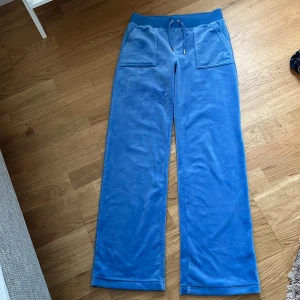 Blå mjukisbyxor från Juicy Couture - Säljer ett par superbekväma blå mjukisbyxor från Juicy Couture i storlek S. Byxorna har använts Max 2 gånger har annars bara suttit i garderoben. De har en elastisk midja med snörning och praktiska fickor både fram och bak. Perfekta för en avslappnad dag hemma eller en chill dag ute!Säljer dessa då dom bara tar plats i garderoben. Ursprungpris: 1000kr (vi kan komma överens över ett rimligt pris)