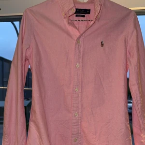 Polo Ralph Lauren Skjorta - Sjukt snygg Polo Ralph Lauren skjorta, den är i rosa färg och är helt nyskick.  Inga Defekter, Cond 10/10, Storleken är XS i herr storlek i Custom Fit men den sitter som storlek S.     Hör jätte gärna av er vid frågor eller mer bilder! 