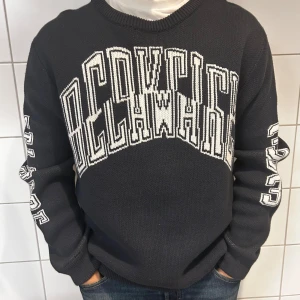 Svart stickad tröja från Dsquared2 - Säljer en snygg svart stickad tröja från weekday Den har ett coolt vitt tryck på framsidan och ärmarna. Perfekt för höst och vinter, och den är superbekväm att ha på sig. Passar både till vardags och lite mer avslappnade tillfällen.