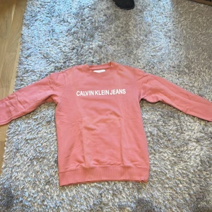 Rosa sweatshirt från Calvin Klein Jeans - Säljer en snygg rosa sweatshirt från Calvin Klein Jeans. Den har en klassisk design med vit logga på framsidan. Tröjan är långärmad och perfekt för både vår och höst. Den är i bra skick och superbekväm att ha på sig. Perfekt för en casual look!