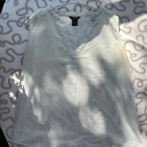 Vit ärmlös topp från Lindex - Säljer en stilren vit ärmlös topp från Lindex. Perfekt för sommardagar eller som ett basplagg i garderoben. Toppen har en v-ringad design och är gjord i ett lätt och bekvämt material.