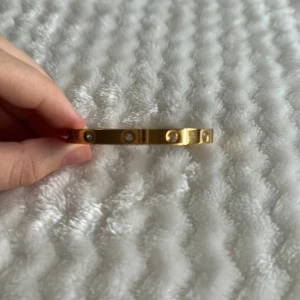 Guldarmband med stenar. - Armbandet har en rund, fast form och är dekorerat med fler jämnt fördelade små stenar. Denna armbanden är inte äkta, men är rostfritt.