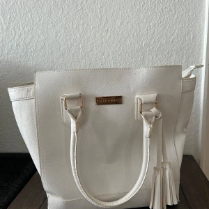 Holly and whyte väska - En vit väska med guld detaljer av holly and whyte. Rymlig väska med två innefickor en som passar din mobil och en annan större med dragkedja. Blå vit detaljer innuti. 