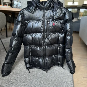 RL Puffer jacket Svart  - Glossy meterial, fin skick, varsamt använt, köpt från HEDE Fashion outlet i Kungsbacka 2023. Har bara haft en ägare (jag). Mindre i storleken än vad man tror (jag brukar ha S/M denna är L. Ända defekten: ett litet hål på höger arm, ÄR LAGAT!  