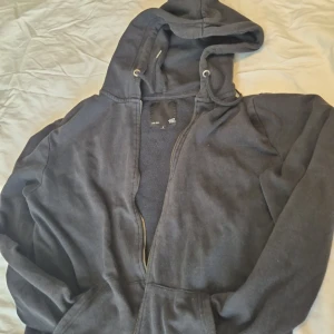 Svart hoodie från 157 - Säljer en svart hoodie från märket 157. Den är i storlek S och har en dragkedja framtill. Perfekt för en chill dag eller när du bara vill vara bekväm. Den har långa ärmar och en skön huva. Passar till allt och är ett måste i garderoben!