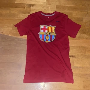 Röd FC Barcelona t-shirt från Nike - Säljer en snygg röd FC Barcelona t-shirt från Nike. Den har en stor klubbemblem på framsidan och är i slim fit-modell. Perfekt för alla Barca-fans!❤️💙       T-shirten är kortärmad och i bra skick, den har bara testats👍