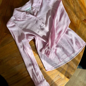 Skjorta - En ljusrosa skjorta med långa ärmar och en klassisk krage. Skjortan har en knappstängning framtill och är tillverkad i ett tunt, lätt tyg! 