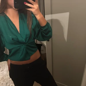 Grön omlottopp - Säljer en snygg grön omlottopp med långa ärmar. Toppen är croppad och har en djup v-ringning, perfekt för en utekväll eller fest. Den är i ett mjukt och bekvämt material som känns skönt mot huden.