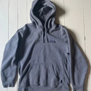 Grå hoodie från Patagonia - Säljer en supermjuk och bekväm grå hoodie från Patagonia. Perfekt för kyliga dagar med sin klassiska design och praktiska ficka framtill. Den har en justerbar huva med dragsko och är i riktigt bra skick. Passar perfekt för både vardag och äventyr!