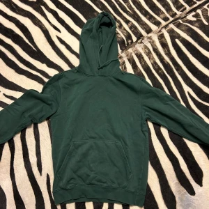 Grön hoodie från Weekday - Säljer en snygg grön hoodie från Weekday. Den är perfekt för  chill. Hoodien har en klassisk design med en stor ficka fram och en bekväm huva. Materialet är mjukt och skönt, vilket gör den idealisk för kyliga dagar.   