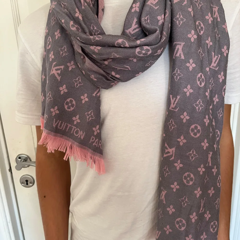 Säljer en superfin grå och rosa halsduk från Louis Vuitton. Den har ett klassiskt monogrammönster och är perfekt för att ge lite lyx till din outfit. Halsduken är mjuk och skön, perfekt för kyliga dagar. Den har fransar i kanterna som ger en extra touch av stil.. Muu.