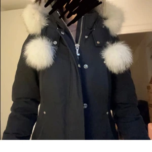 Svart parkajacka från Moose Knuckles - Säljer en snygg och varm svart parkajacka från Moose Knuckles. Jackan har en fluffig vit päls.  Den är perfekt för kalla vinterdagar och har en dragkedja samt knappar. Välskött inga skador eller hål. Pris diskuteras