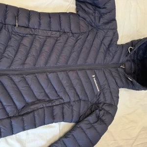 Mörkblå dunjacka från Peak Performance - Säljer en snygg och varm mörkblå dunjacka från Peak Performance. Perfekt för kalla vinterdagar med sin långa ärm och dragkedja. Jackan har en stilren design och är i bra skick. Passar perfekt för både vardag och utomhusaktiviteter.