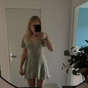 Klänning blommig - Ljus grön klänning med blommor säljs för jag tycker den blivit för kort på mig ( är 180lång). Men fin klänning i bra skick som knyts i midjan och har volang 
