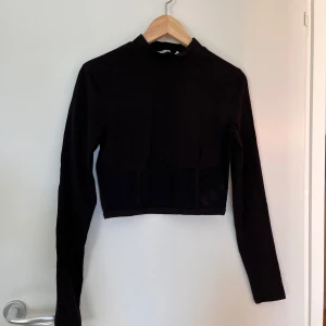 Svart croppad topp från NA-KD - Säljer en snygg svart croppad topp från NA-KD. Den har långa ärmar och en cool mesh-detalj i nederkanten som ger en extra edge. Perfekt för både vardag och fest! 🖤