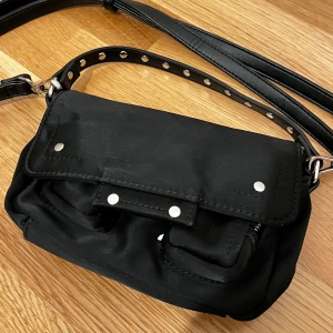 Núnoo Honey Bag - Núnoo Axelremsväska i svart färg. Jättefin och söt men kommer inte till användning längre. I bra skick!