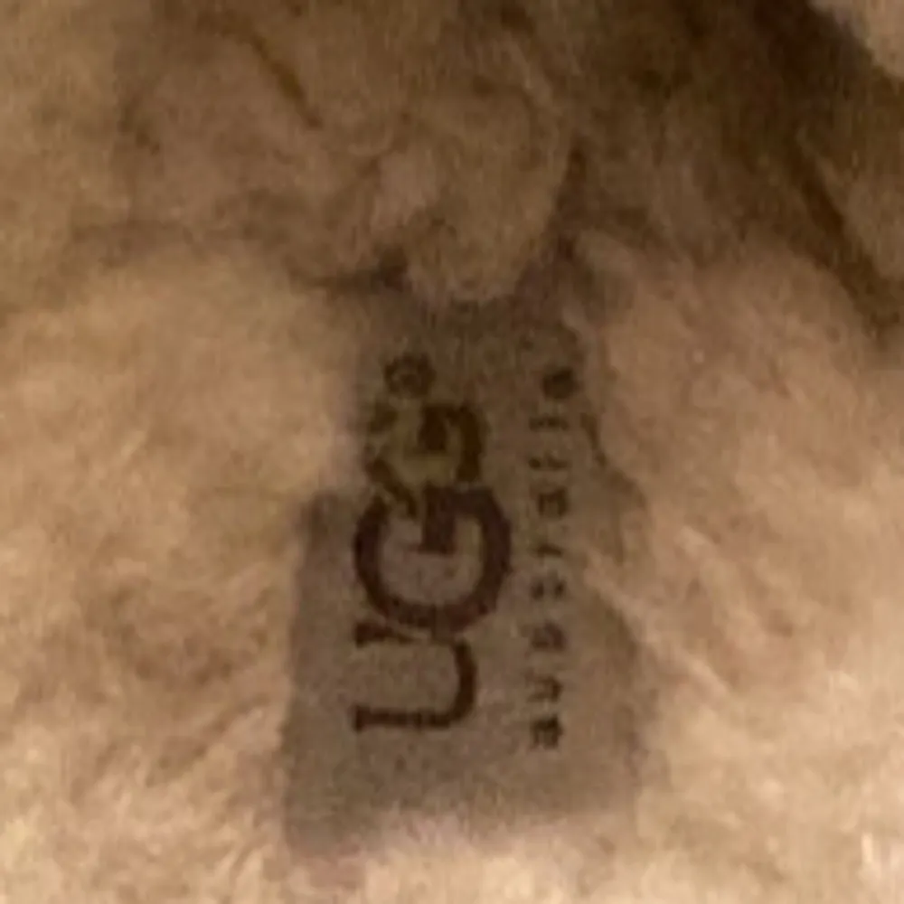 Mysiga och varma beige tofflor från UGG med fluffigt foder. Perfekta för kalla dagar hemma. De har en klassisk design med rundad tå och är gjorda i mjukt material för extra komfort.. Skor.