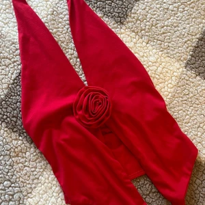 Röd halterneck topp med rosett, storlek S - Snygg röd halterneck topp med en dekorativ rosett framtill. Toppen har en stilren design och är tillverkad i ett mjukt material. Använd en gång och i storlek S.