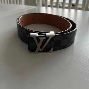 Rutig bälte - Säljer ett snyggt bälte med ett rutigt mönster i brunt och svart. Bältet har ett stilrent svart spänne och är i nytt skick. Perfekt för att ge din outfit en extra touch!