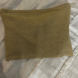 Guldig tubtopp från Gina Tricot - Snygg guldig tubtopp från Gina Tricot. Perfekt för en glittrig look med sin skimrande yta. Enkel och stilren design som passar till många olika outfits.