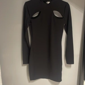 Svart klänning med cut-outs - Snygg svart klänning med lång ärm och trendiga cut-outs vid axlarna. Perfekt för en kväll ute eller en speciell tillställning. Den har en tight passform som framhäver figuren.