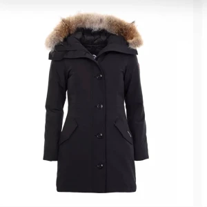 Svart parkajacka med pälsdetalj - Snygg svart parkajacka med avtagbar huva och pälsdetalj. Jackan har långa ärmar och knäppning framtill med stora knappar. Perfekt för kalla dagar med sin varma och skyddande design.