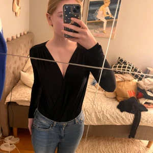 Svart omlottbody från H&M - Snygg svart omlottbody från H&M i storlek S. Långa ärmar och en djup v-ringning. Tunnt och glansigt material. Knappt använd.