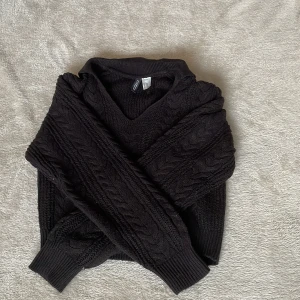 Svart stickad tröja från Divided - Säljer en svart stickad tröja från Divided med ett klassiskt flätmönster. Tröjan har en v-ringad hals och långa ärmar, perfekt för kyligare dagar. Den är både stilren och bekväm, ett måste i garderoben!