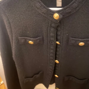 Svart kavaj med guldknappar - Snygg svart kavaj med guldknappar framtill och dekorativa fickor. Den har en klassisk design med långärmade ärmar och en elegant look. Perfekt för att ge en stilren touch till din outfit.