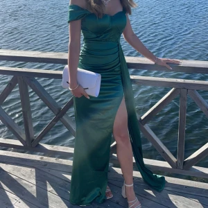Grön bal/festklänning med slits  - Elegant grön långklänning i satin med offshoulder-design och en slits framtill. Klänningen har en figurnära passform som framhäver silhuetten. Har använt endast en gång. Den har dessutom en inbyggd bh och har otroligt bra material! Vid frågor är det bara att höra av sig💚