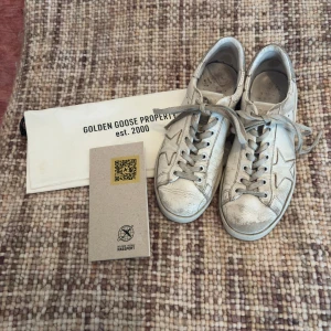 Vita sneakers från Golden Goose - Snygga vita sneakers från Golden Goose med en stjärndetalj på sidan och glittrig häl. Skorna har snörning och en klassisk design men de är däremot väldigt slitna därav priset. Äktighets bevis och Dustbag ingår💕 nypris ca: 5500kr storleken är 38 men passar mig som är 37 pris kan diskutera