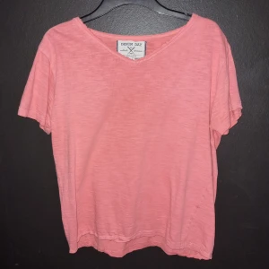 Korall t-shirt från Denim Day - Säljer en snygg korall t-shirt från Denim Day. Den har en avslappnad passform och är kortärmad med en v-ringad hals. Perfekt för en casual look.