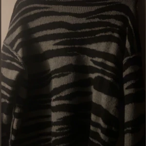 Svart och grå zebramönstrad tröja - Säljer en svart och grå zebramönstrad tröja med långa ärmar. Perfekt för att ge en djärv touch till din outfit. Tröjan har en bekväm passform och är idealisk för kyligare dagar.