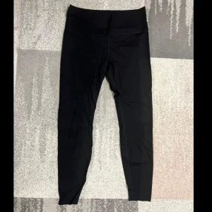 Svarta leggings med textdetalj - Snygga svarta leggings med hög midja och texten 'MOVE IT' i färgglada bokstäver på baksidan av midjan. Perfekta för träning eller en avslappnad dag. De är tillverkade i ett stretchigt material som ger en bekväm passform.