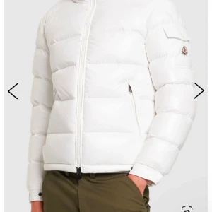 Vit dunjacka från Moncler - Säljer en stilren vit dunjacka från Moncler. Jackan har en dragkedja framtill och långa ärmar. Den är perfekt för kyligare väder och har en klassisk pufferdesign med Moncler-logotyp på ärmen.