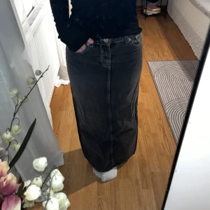 Svart långkjol i jeansmaterial - Snygg svart långkjol i jeansmaterial med klassisk femficksdesign. Kjolen har en rak passform och är perfekt för en stilren look. Den är enkel att matcha med olika toppar och accessoarer. Helt oanvänd 🌼
