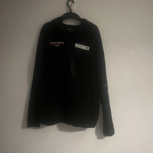 Svart hoodie från Hoodrich - Säljer en svart hoodie från Hoodrich med tryck på både fram- och baksidan. Hoodien har en dragkedja framtill och är i storlek M. Perfekt för en casual look. Ps den har ett litet hål på högra sodan på baksidan