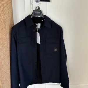 Ny mörkblå overshirt från Les Deux - Ny varm och  stilren mörkblå overshirt i ull från Les Deux. Storlek XS, nypris 1399 kr. Den har knappar framtill och två bröstfickor med lock. Perfekt för lager-på-lager-stil och ger en snygg touch till din outfit.