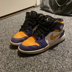 Nike Air Jordans 1 Lakers storlek 37,5 - Säljer ett par Nike Air Jordans 1 Lakers i storlek 37,5 med en cool färgkombination av lila, gult och vitt. Skorna har den klassiska snörningen och en bekväm passform. Perfekta för dig som vill ha en stilren och sportig look.