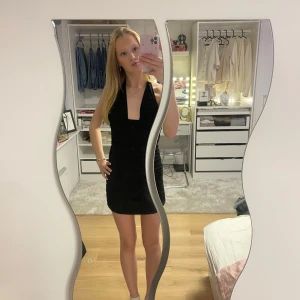 Svart kortklänning med öppen rygg - Snygg svart kortklänning med en lång v-ringning och öppen rygg. Klänningen har en tight passform och är perfekt för en kväll ute. Den är ärmlös och har en elegant rynkad detalj på baksidan. 