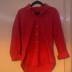 Röd skjorta från Ralph Lauren - Snygg röd skjorta från Ralph Lauren med klassisk krage och knappar framtill. Den har en broderad logga på bröstet i blått. Skriv vid intresse! Storlek: S