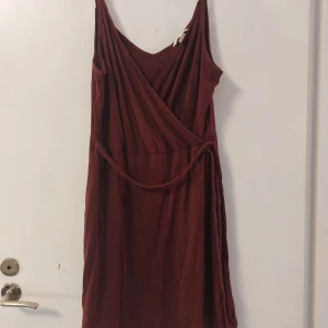 Vinröd omlottklänning från H&M - Säljer en vinröd omlottklänning från H&M i storlek M. Klänningen har en v-ringad design och knytband i midjan för en smickrande passform. Tillverkad av en mjuk blandning av bomull och modal, går till strax övan knäna